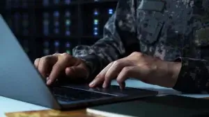 a close-up photo of hands of a solider typing on a laptop keyboard